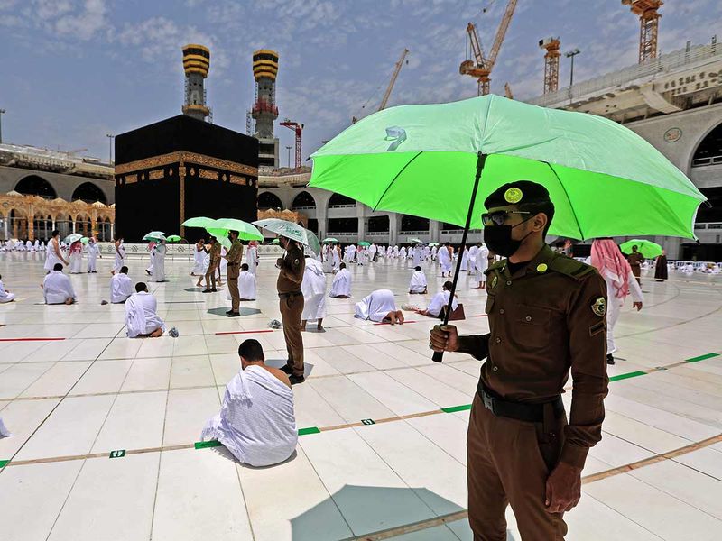 Members of the Saudi security forces holding umbrellas stand guard, as worshippers pray around the Kaaba in the Grand mosque complex in the Saudi city of Mecca, during the Friday prayers of the Muslim holy fasting month of Ramadan, on April 16, 2021. 